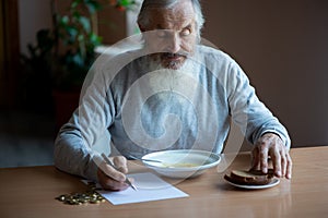 Senior  man counting money and plans to buy grocery while sitting at an empty soup plate