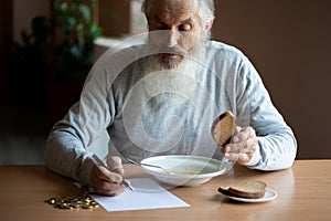 Senior  man counting money and plans to buy grocery while sitting at an empty soup plate