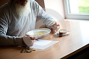 Senior  man counting money and plans to buy grocery while sitting at an empty soup plate