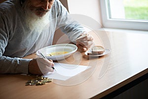 Senior  man counting money and plans to buy grocery while sitting at an empty soup plate