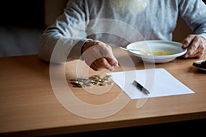 Senior  man counting money and plans to buy grocery while sitting at an empty soup plate