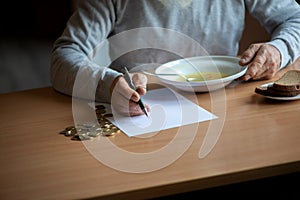 Senior  man counting money and plans to buy grocery while sitting at an empty soup plate