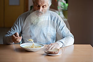 Senior  man counting money and plans to buy grocery while sitting at an empty soup plate