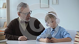 Senior man criticizing grandson, boy in earphones ignoring him, generation gap