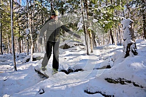Senior Man Crossing a Fallen Log on snowshoes in forest