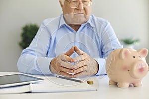 Senior man at desk with notebook, tablet and piggy bank managing personal finance