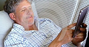 Senior man with digital tablet lying on sofa on the porch 4k