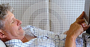 Senior man with digital tablet lying on sofa on the porch 4k