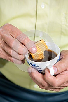 Senior man dips a cookie in his coffee