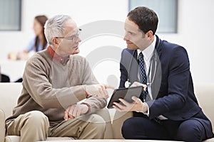 Senior Man Discussing Results With Doctor On Digital Tablet