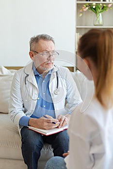 Senior man doctor examining yound woman in doctor office or at home. Girl patient and doctor have consultation in