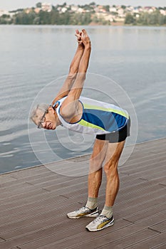 Senior man does a warm-up on the lake embankment