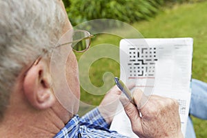 Senior Man Doing Crossword Puzzle In Garden