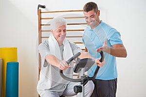 Senior man doing exercise bike with his trainer