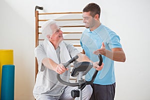 Senior man doing exercise bike with his trainer