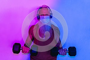 Senior man doing gym workout with dumbbells while wearinf face protective mask during Coronavirus isolation quarantine - Fitness,