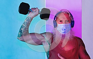 Senior man doing gym workout with dumbbells while wearing face protective mask during Coronavirus isolation quarantine - Fitness,