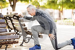 Senior man doing stretching workout on a park bench