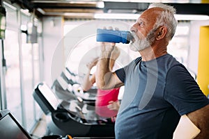 Senior man drinking bottle of water on threadmill in gym