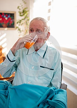 Senior man drinking juice in wheelchair at home