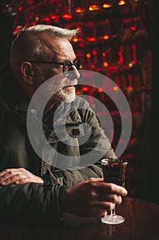 Senior man drinking red liquor in a pub, relaxing at the counter. Hide from problems in a bar with alcohol