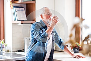 Senior man drinking water in the kitchen.