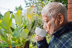 A senior man drinks coffee morning while standing in a garden. Concept of aged people and relaxation