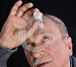 Senior man dripping a red bloodshot eye with eye drops