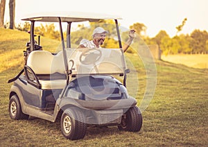 Senior man driving golf car and waving