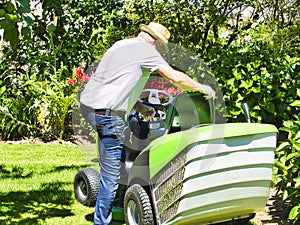 Senior man driving a tractor lawn mower in garden with flowers