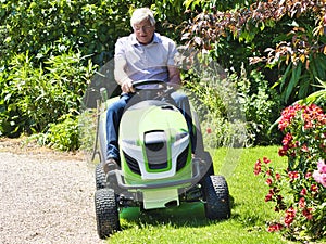 Senior man driving a tractor lawn mower in garden with flowers