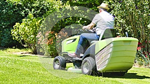 Senior man driving a tractor lawn mower in garden with flowers