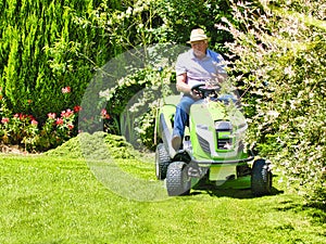 Senior man driving a tractor lawn mower in garden with flowers