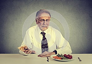 Senior man eating fresh vegetable salad avoiding fatty pizza. Healthy diet nutrition choices concept