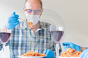 Senior man is eating italian spaghetti pasta during or after corona virus outbreak, with personal protective equipment