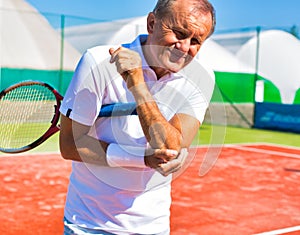 Senior man with elbow pain standing during tennis match on sunny day