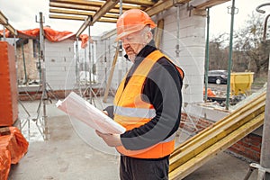 Senior man engineer or construction worker in hardhat looking at blueprints at building new modern house. Male architect or