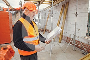 Senior man engineer or construction worker in hardhat looking at blueprints at building new modern house. Male architect or