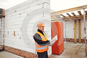 Senior man engineer or construction worker in hardhat looking at blueprints at building new modern house. Male architect or