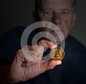 Senior man examining a bitcoin at arms length