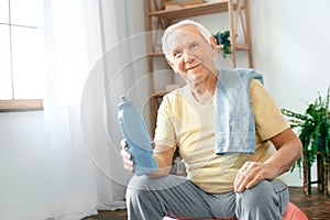 Senior man exercise at home sitting on exercise ball rest drinking water