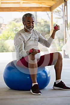 Senior man exercising with dumbbells on exercise ball in the porch