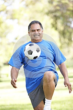 Senior Man Exercising With Football In Park