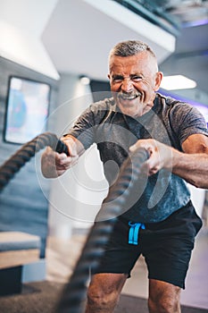 Senior man exercising with ropes at the gym.