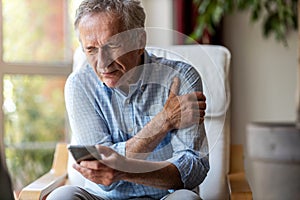 Senior man experiencing pain while using a smartphone photo