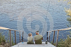 Senior man fishing with grandson, spending time near river, holding fishing rods in hands, to enjoy spending time together,