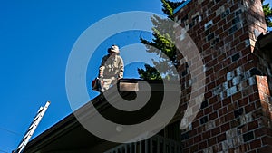 Senior man with gas powered leaf blower cleaning debris out of rooftop gutters