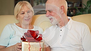 Senior man giving birthday anniversary present golden gift box to wife. Valentine`s Day celebration