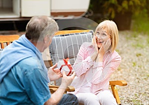 Senior man giving birthday gift to his surprised wife near RV in counryside