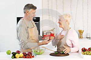 Senior Man Giving Birthday Gift To Wife Standing In Kitchen